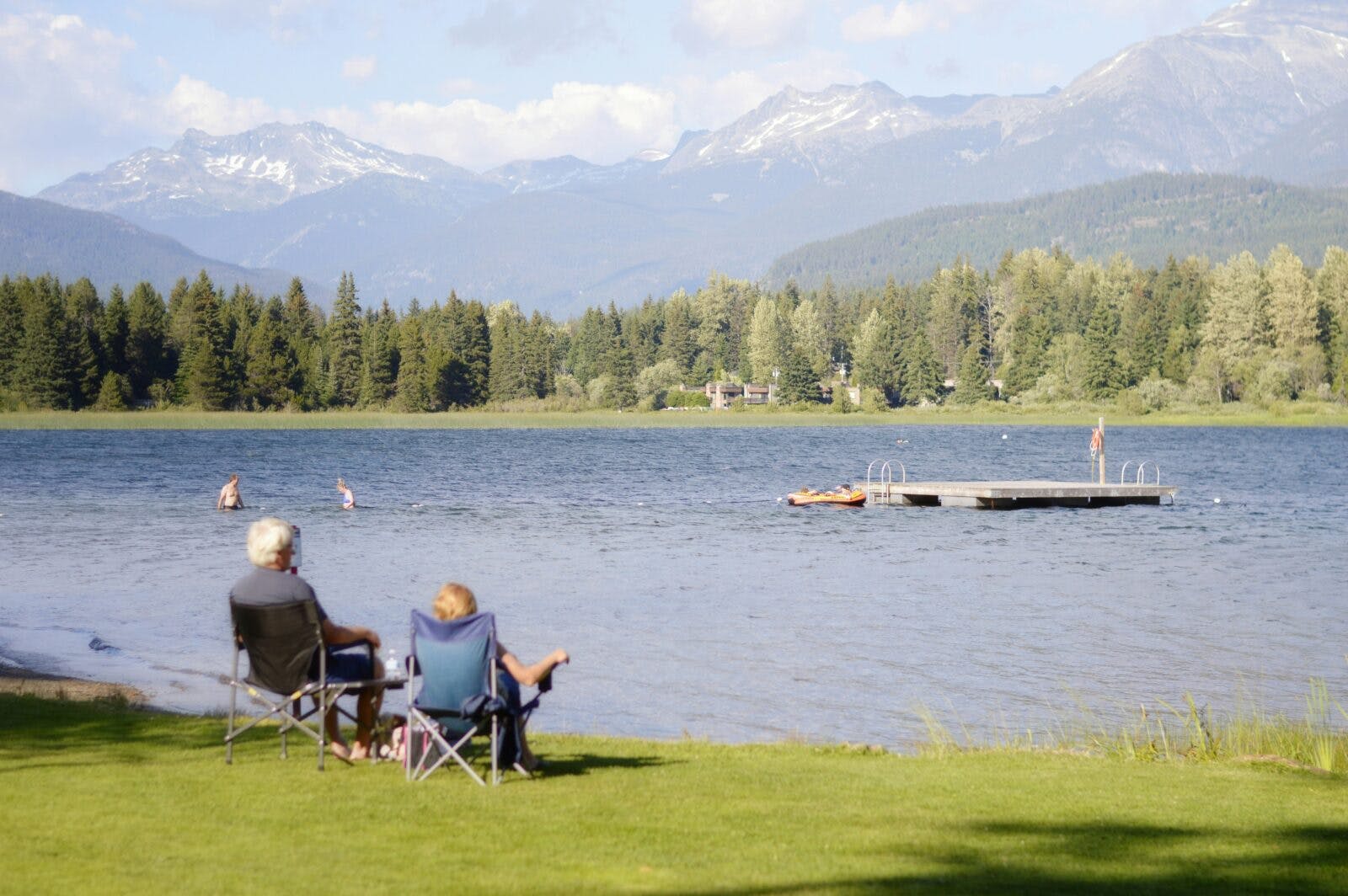 people sitting on the camping chair while looking at others swimming in the lake